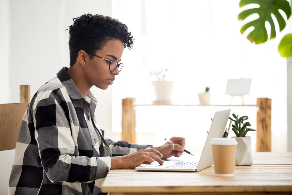 African american young woman using laptop working studying online, serious black girl student worker looking at laptop making notes typing busy on computer research, search information in internet
