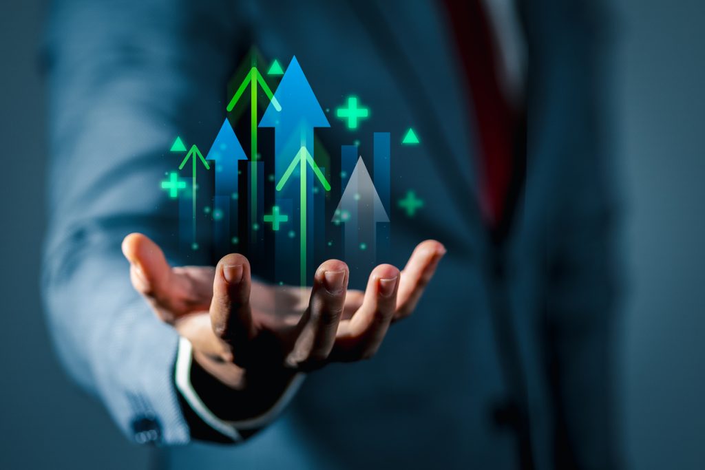 Business growth and success concept with businessman holding rising arrows and positive indicators, symbolizing profit increase, financial progress, investment opportunities, and upward business trends.