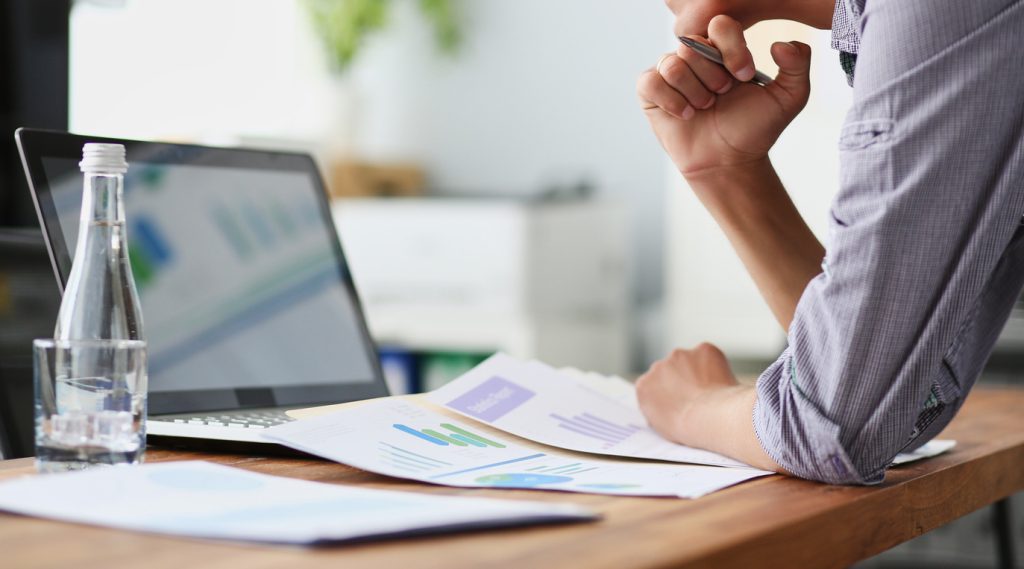 Side view of experienced businessman looking at financial data with graphics and charts while work on a laptop computer. Young entrepreneur analyzing performance on his notebook, male freelancer work in office interior.