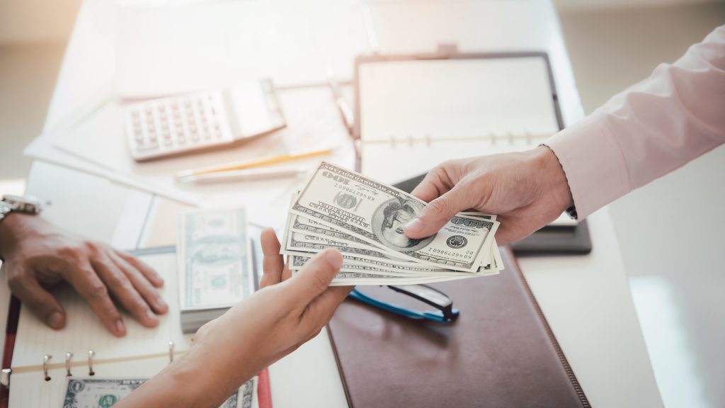 Man offering batch of hundred dollar bills. Hand of a businessman giving money to his partner. Hand receiving money from businessman. Venality, bribe, corruption concept.