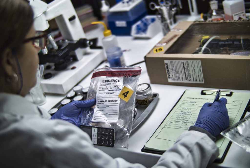 A police forensic expert is examining a mobile phone that is being used as evidence in a murder case